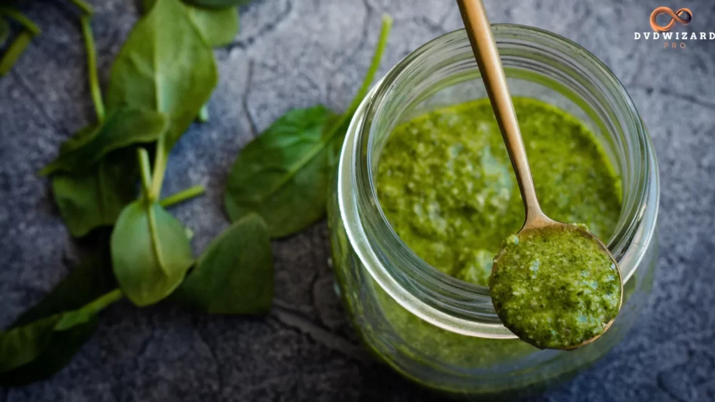 A bowl of Jamaican Green Sauce with fresh basil, parsley, walnuts, garlic, and grated cheese on a wooden table.