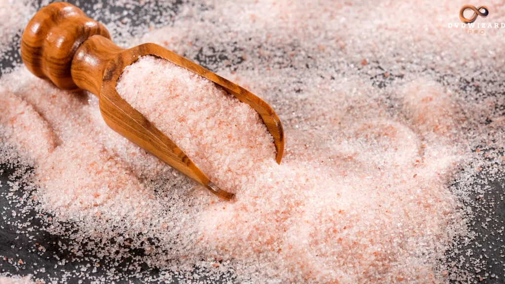 Finely ground pink Tibetan salt in a wooden scoop, spread over a black surface for contrast.