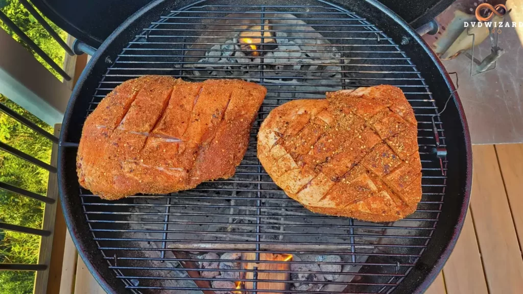 Two seasoned pork butts on a charcoal grill with a crosshatch cut for better fat rendering.