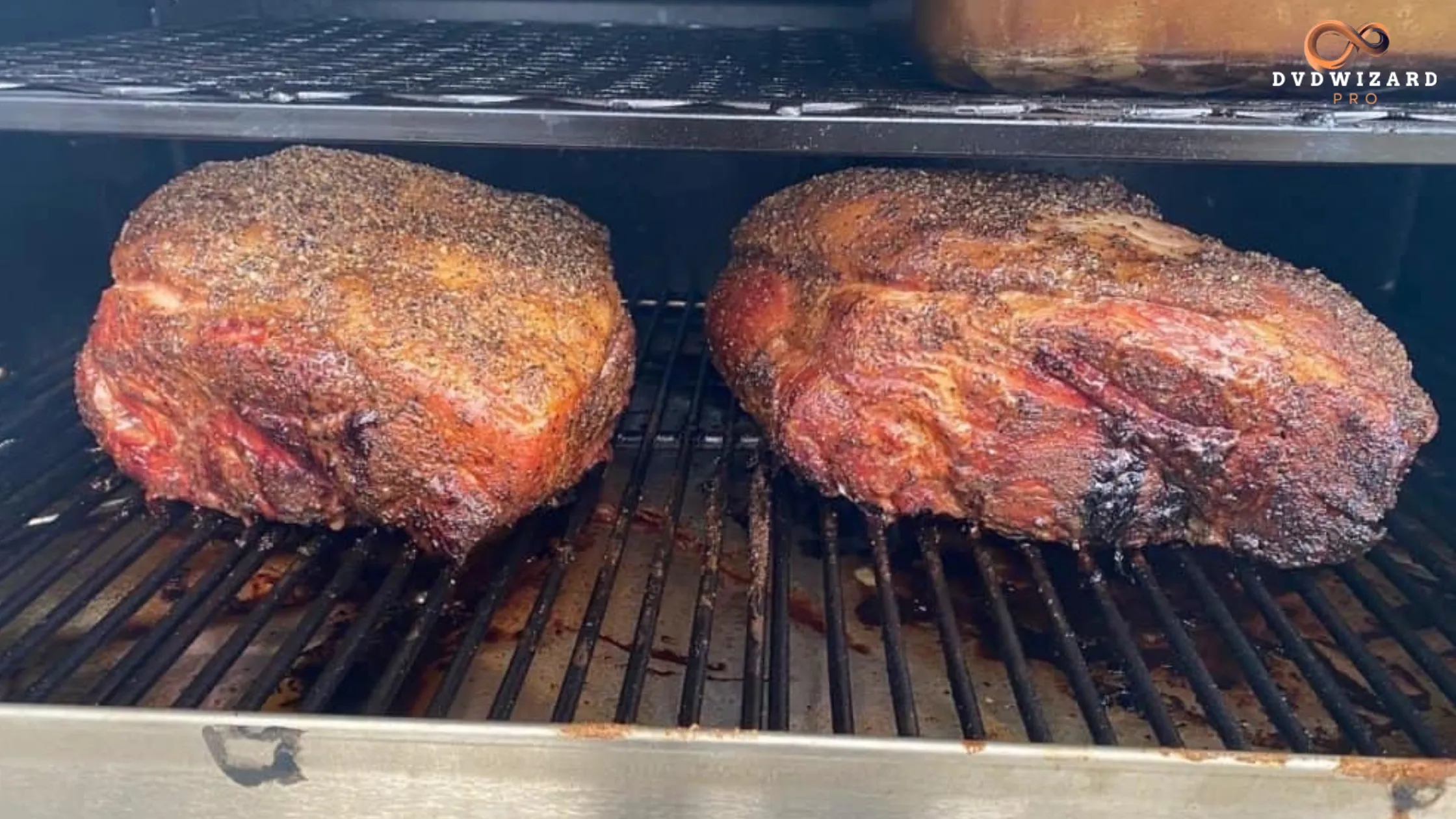 Two seasoned pork butts smoking on a grill with a flavorful crust forming.